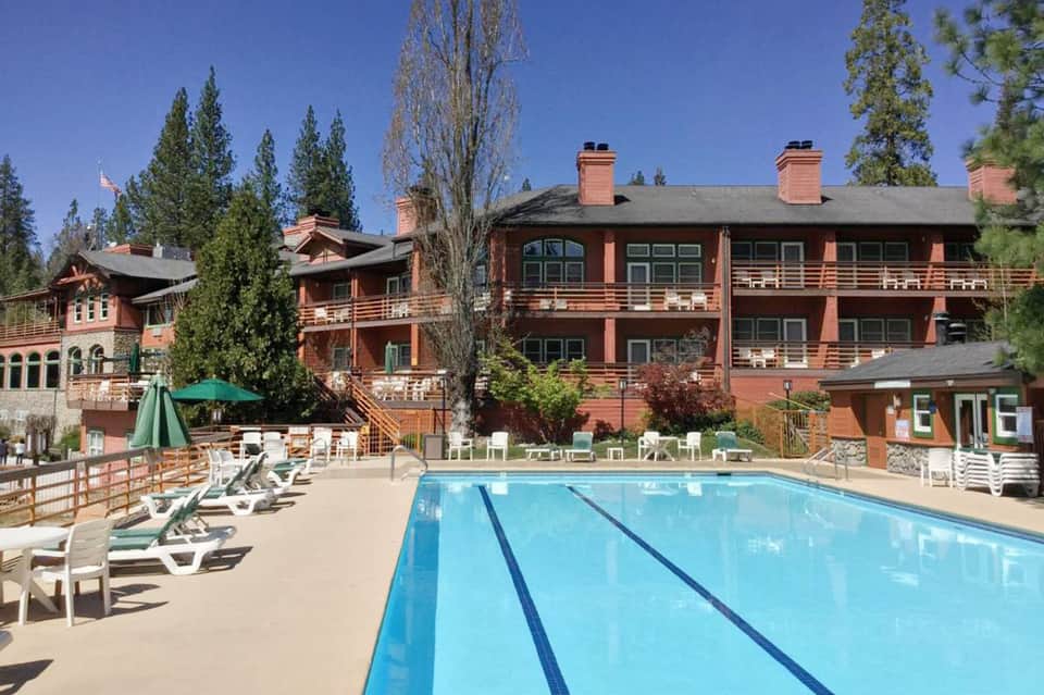 Resort pool with lap lanes and lounge chairs, red-brick lodge buildings, mountain forest backdrop