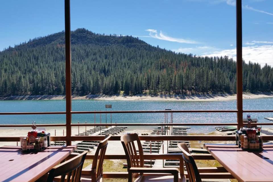 Lakeside dining area with large windows framing forest-covered mountains and pristine blue water