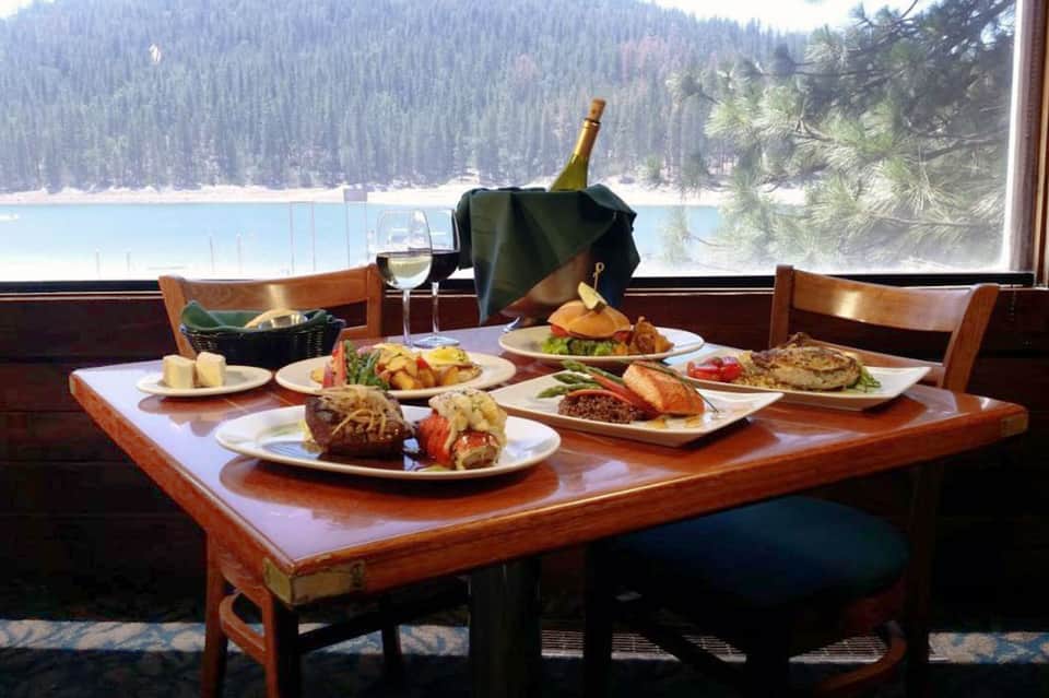 Fine dining table with multiple plates, wine bottle, and mountain lake view through window