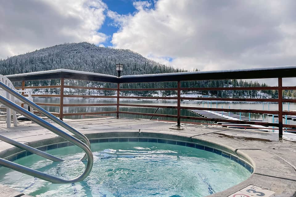 Hot tub on wooden deck with mountain lake and forested landscape views