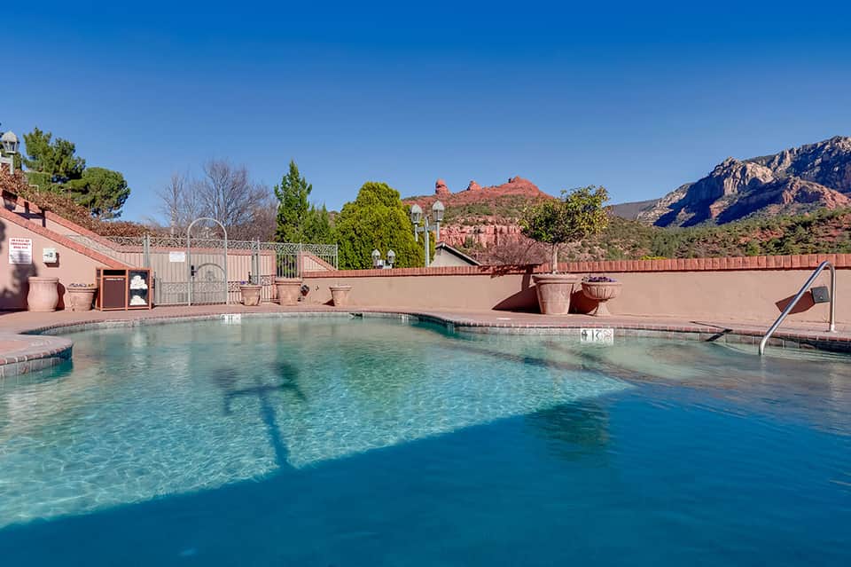 Resort pool surrounded by red clay-colored deck with mountain backdrop and clear blue sky
