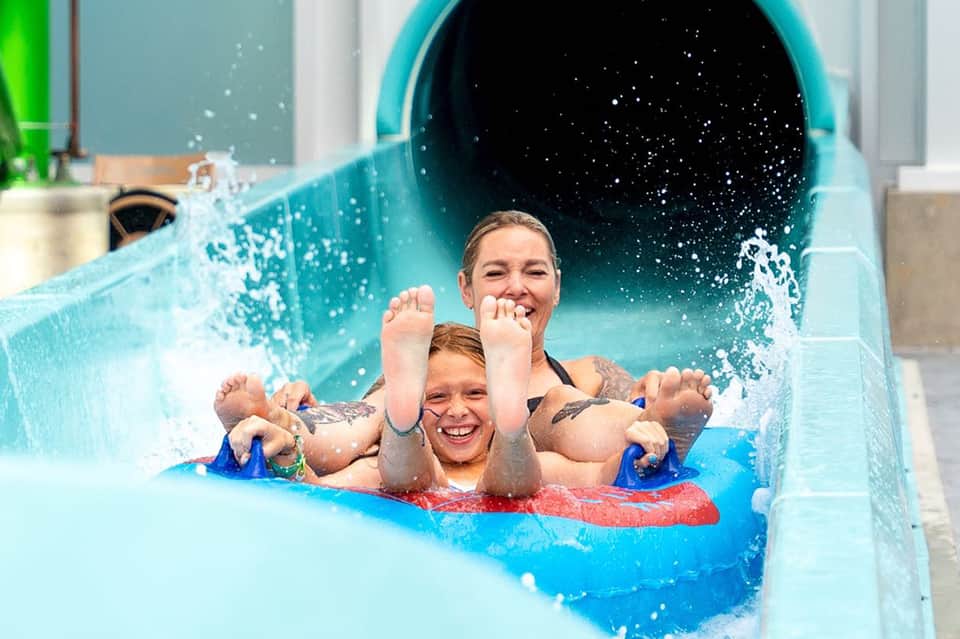 Adult and child on red raft exiting blue water slide with splashing water