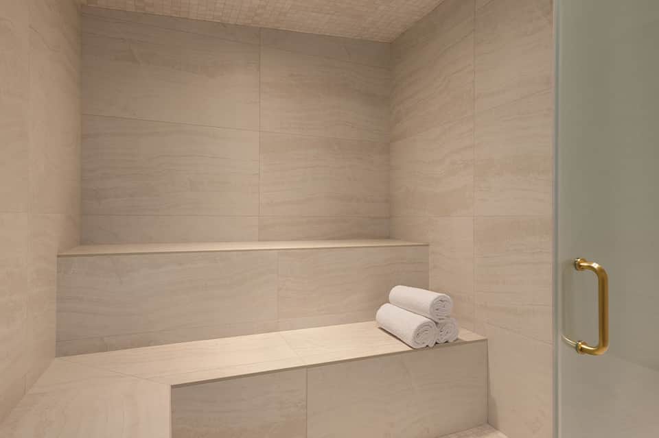Luxurious bathroom with limestone tile steam shower and rolled white towels