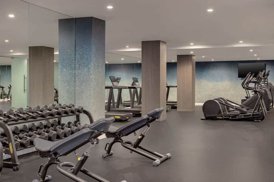 Modern hotel fitness center with dumbbells, cardio equipment, and columns