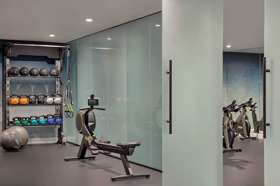 Contemporary fitness center with exercise bikes, weights, and mirrored glass partitions