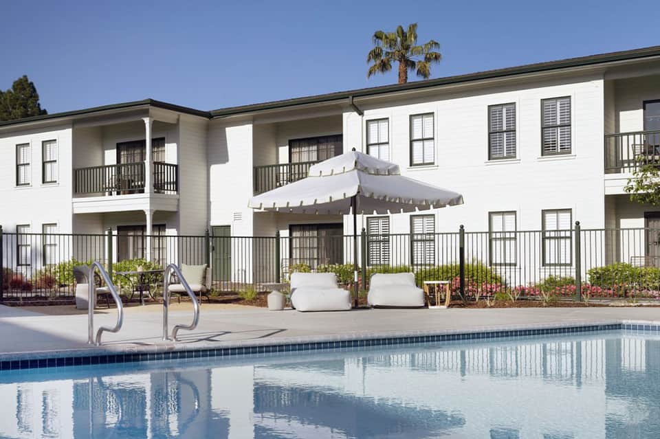 Modern white pool cabanas with lounge seating, white umbrella, and residential-style buildings