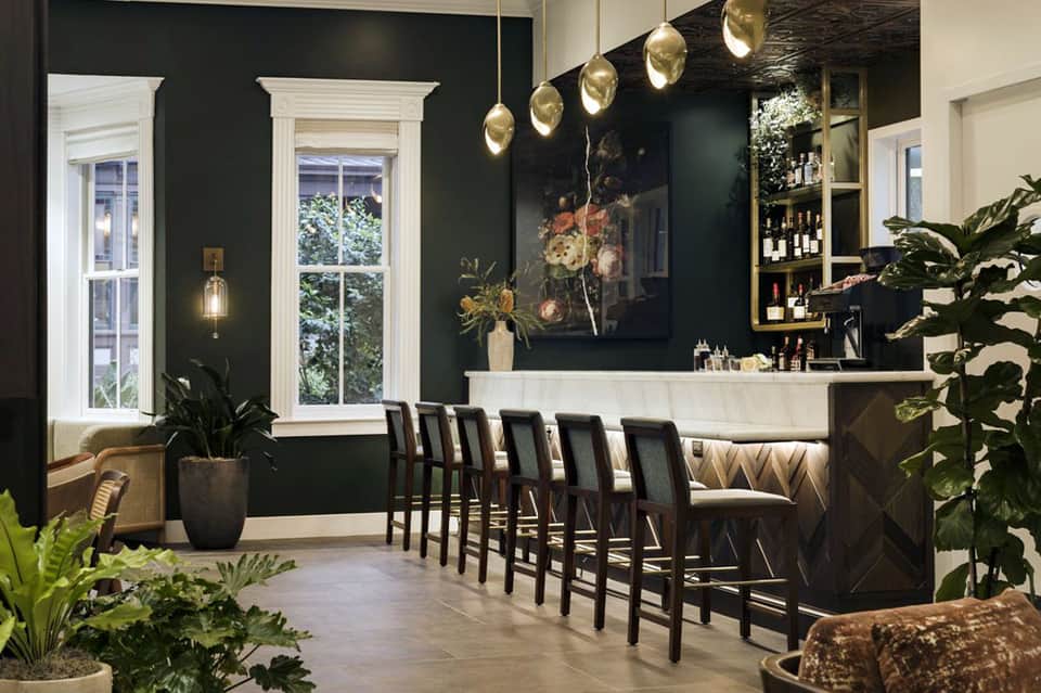 Elegant hotel bar interior with dark green walls, brass pendant lights, and white bar counter
