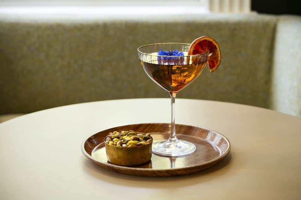 Craft cocktail with orange slice and mixed nuts on white table in modern lounge setting