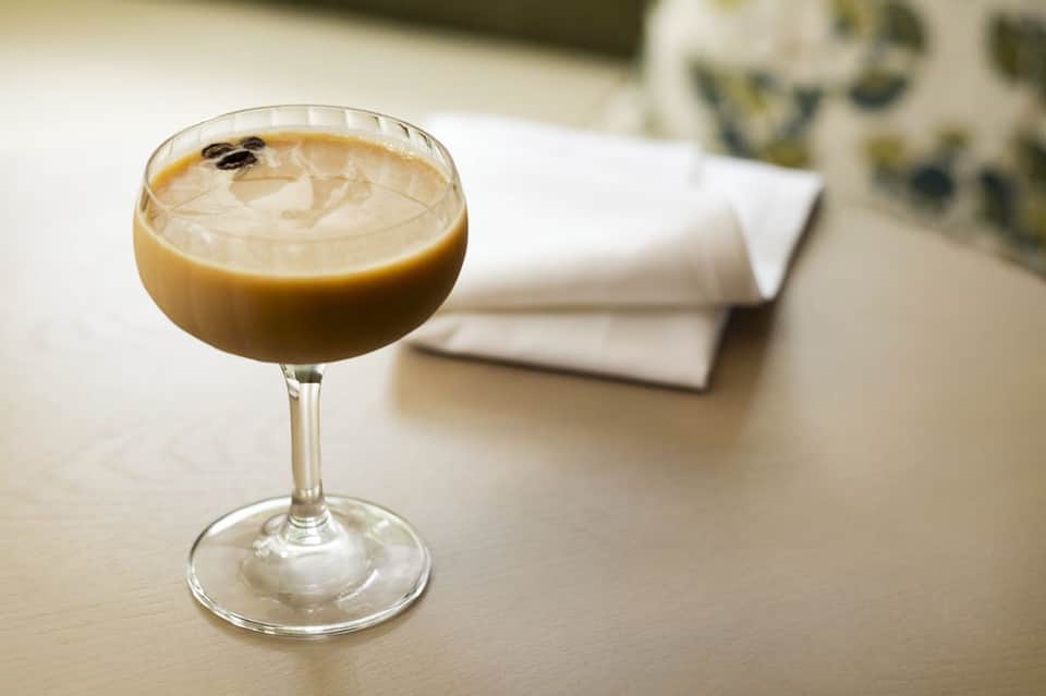 Creamy tan cocktail in coupe glass on light table with blurred background