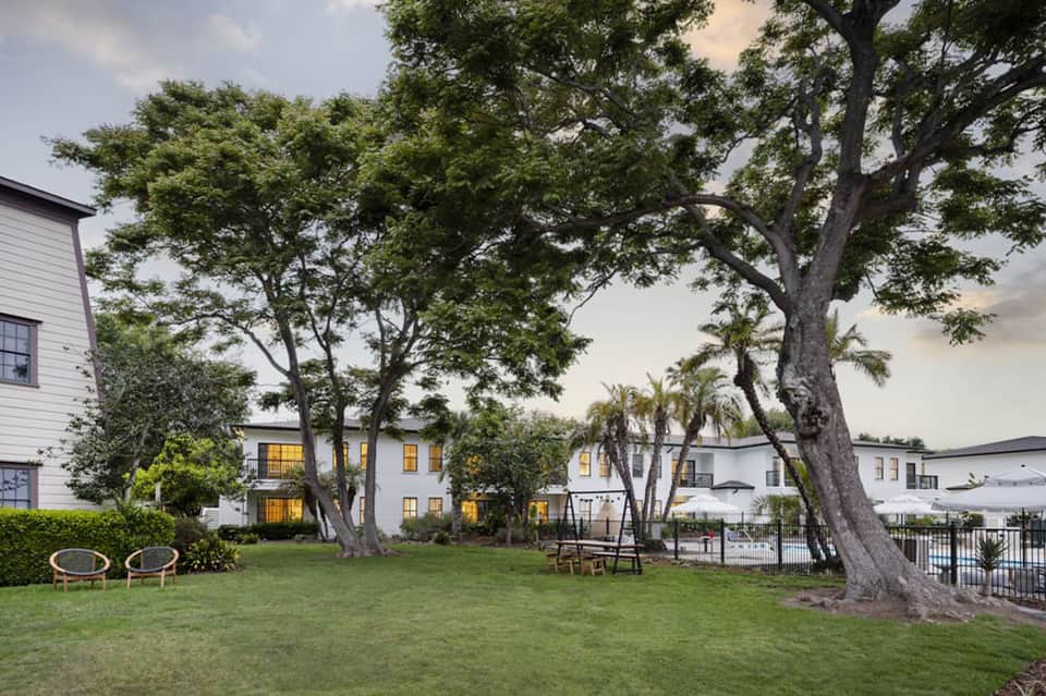 Resort courtyard with mature trees, white buildings, and green lawn at dusk