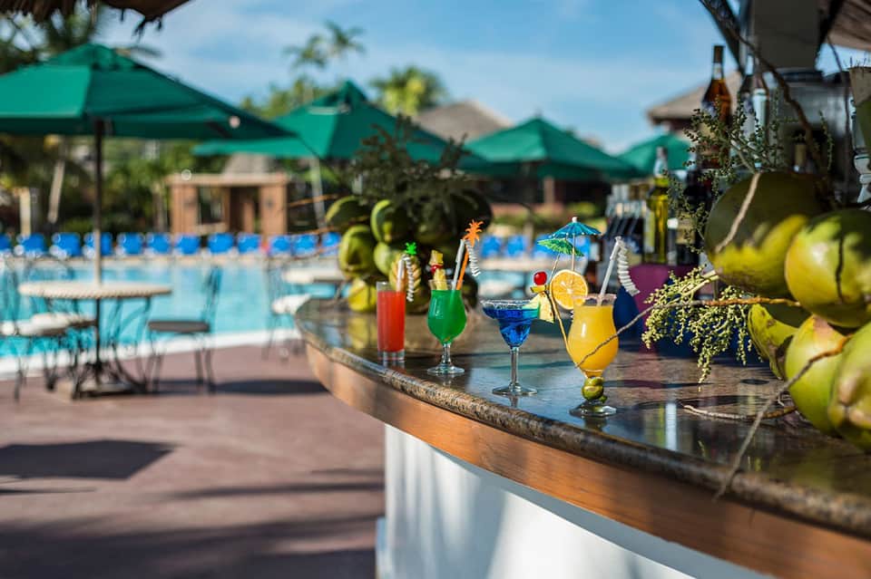 Colorful tropical cocktails on poolside bar with resort and green umbrellas behind