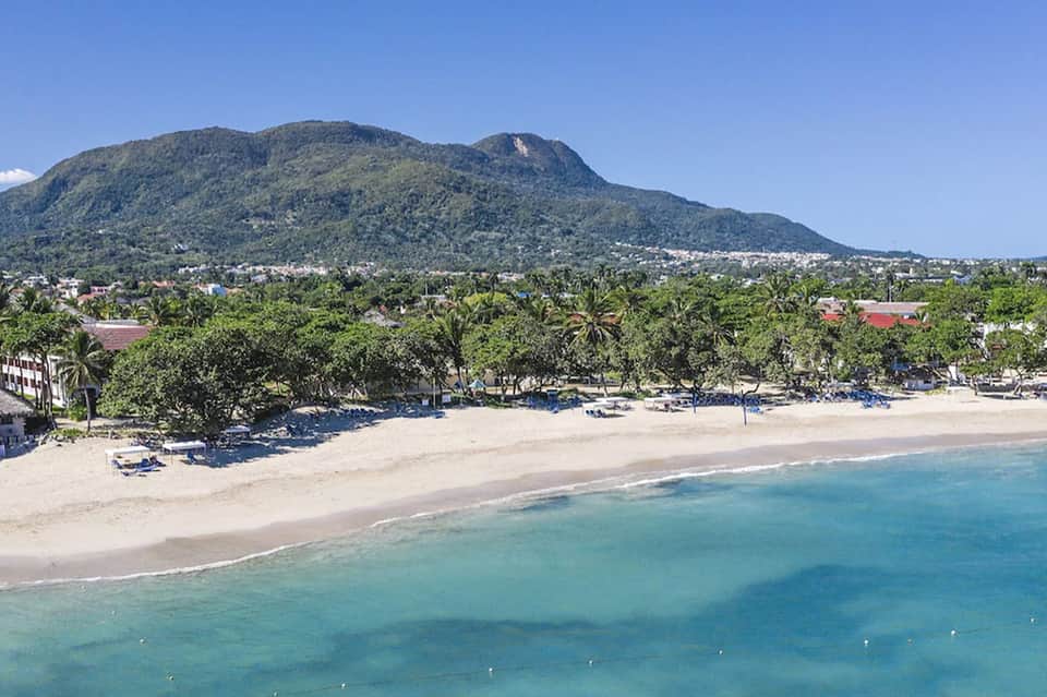 Scenic tropical beach with turquoise waters, palm trees, and green mountain backdrop