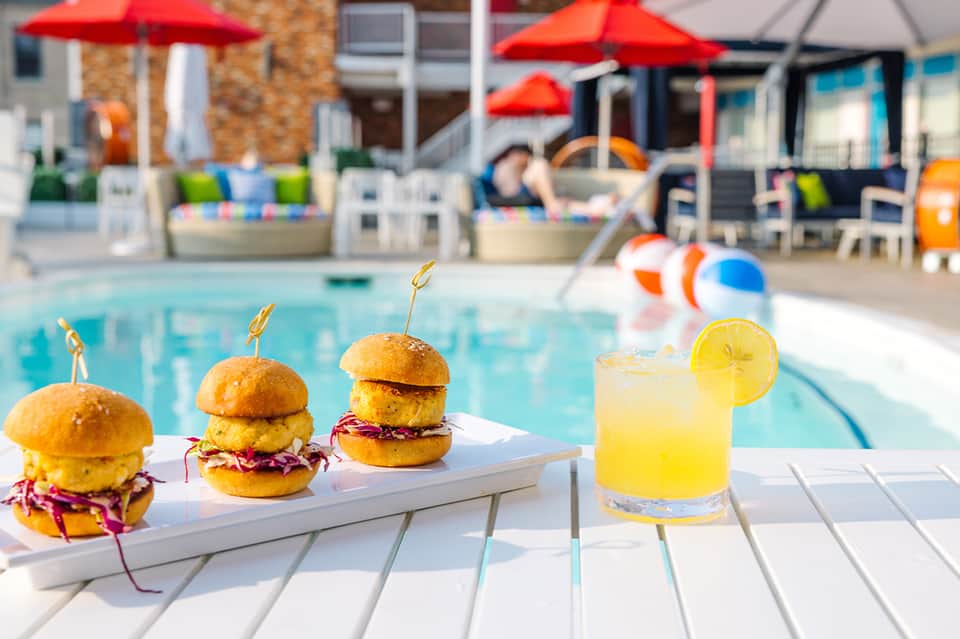 Gourmet sliders and cocktail by resort pool with red umbrellas, loungers, and red umbrellas