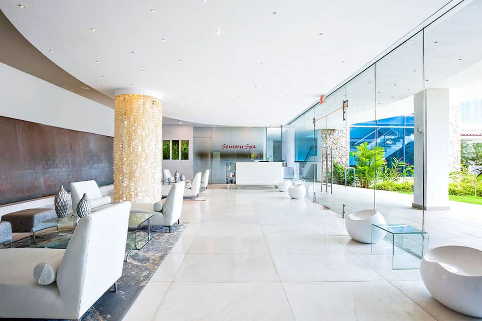 Modern spa reception area with white furniture, golden column, glass partitions, and ocean views