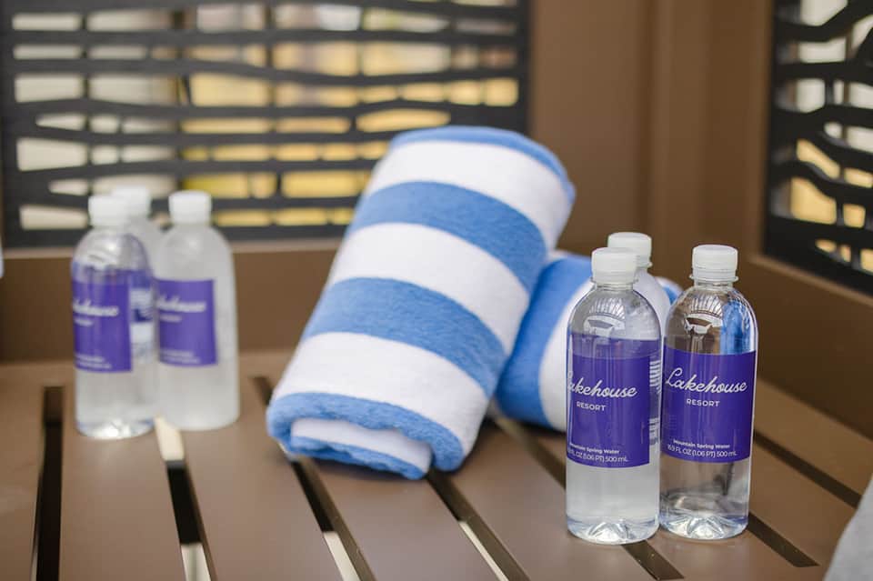 Resort amenities including branded water bottles, towel, and spa products on table with ocean view