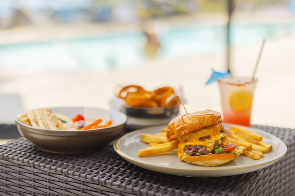 Beach dining setup with cheeseburger, fries, and tropical drinks