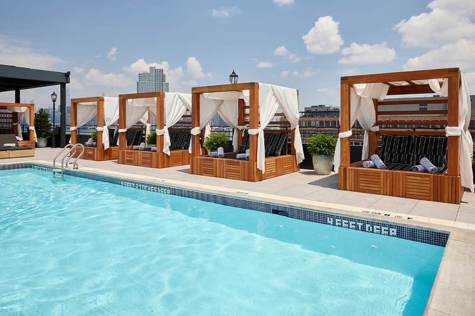 Rooftop pool with wooden cabanas and city skyline view