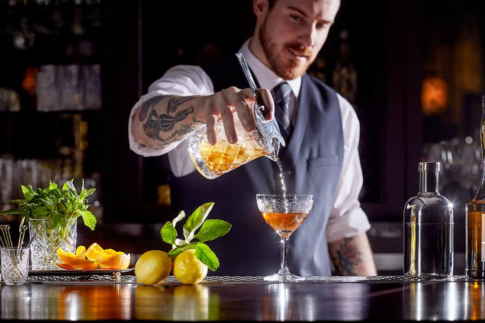 Bartender pouring craft cocktail with fresh citrus and mint garnish at upscale bar