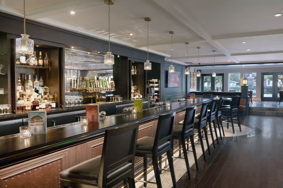 Upscale bar with dark wood accents, pendant lighting, well-stocked shelves, and lounge seating