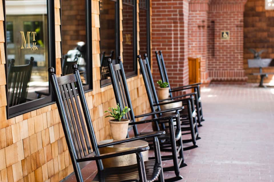Row of black rocking chairs on brick patio outside historic building with windows