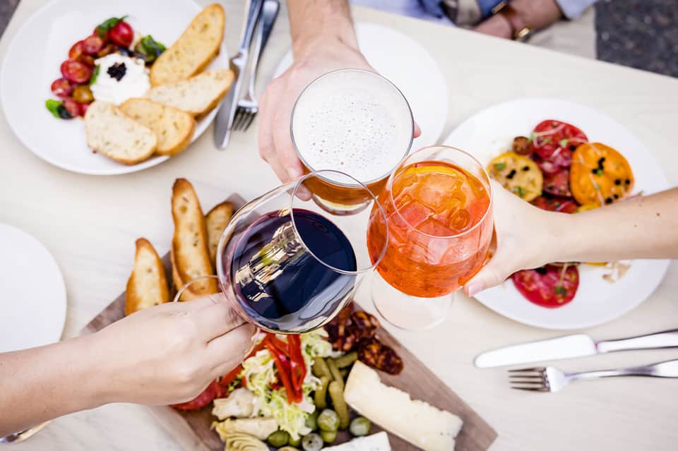 Toast and cheers with three glasses of wine and beverages over dining table with appetizers and fresh fruit plates