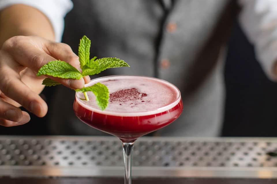 Cocktail with pink-red color, mint garnish, and creamy foam top at hotel bar