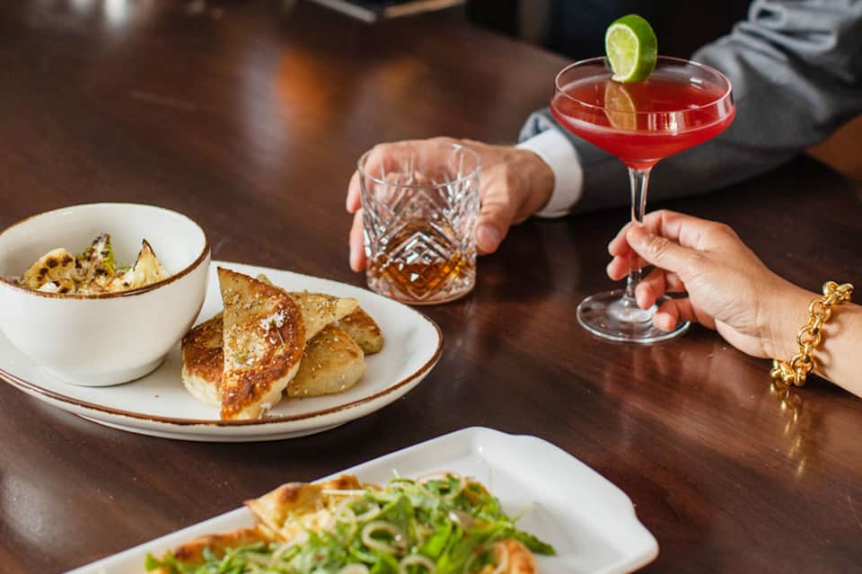 Fine dining scene with cocktail, plated appetizers, and drinks on dark wood table
