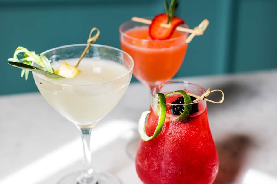 Three artfully crafted cocktails with vibrant colors, fresh garnishes, and tropical presentation