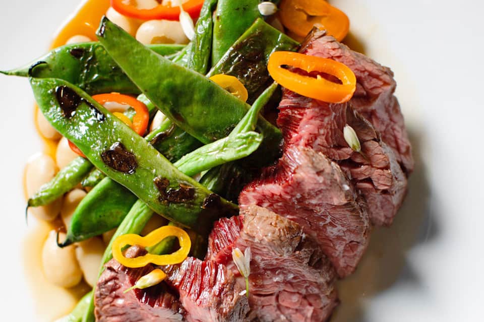 Grilled steak with charred peppers and garnish plated on white surface