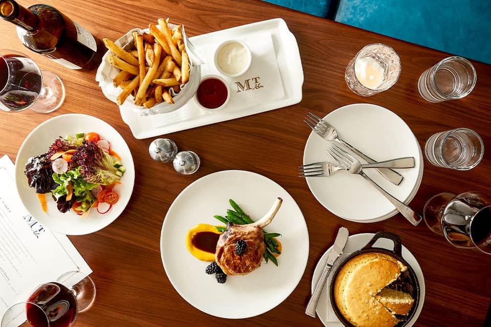 Fine dining table with plated duck, salad, fries, and wine glasses on wooden surface