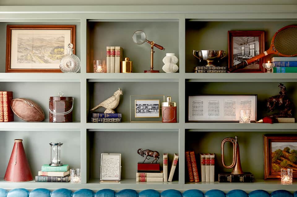 Styled bookshelf displaying decorative objects including books, framed art, sports memorabilia, and vintage collectibles with blue base