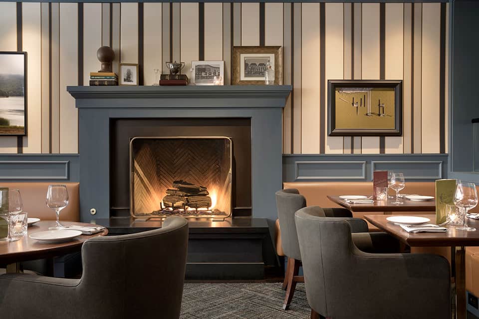 Fine dining restaurant with fireplace, blue-gray walls, earth-tone banquettes, and place settings