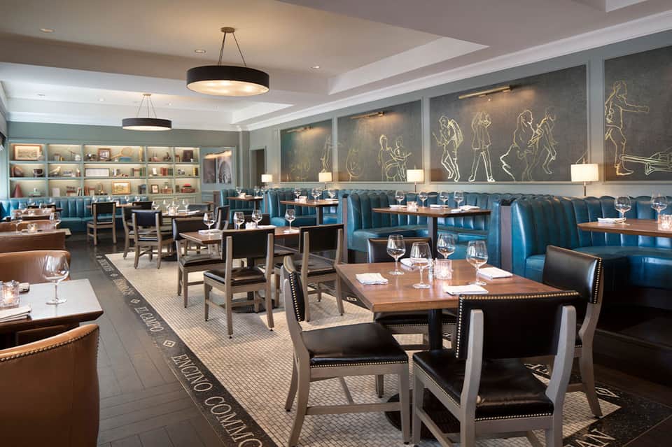 Upscale restaurant with blue booths, wood tables, shelving, and pendant lighting