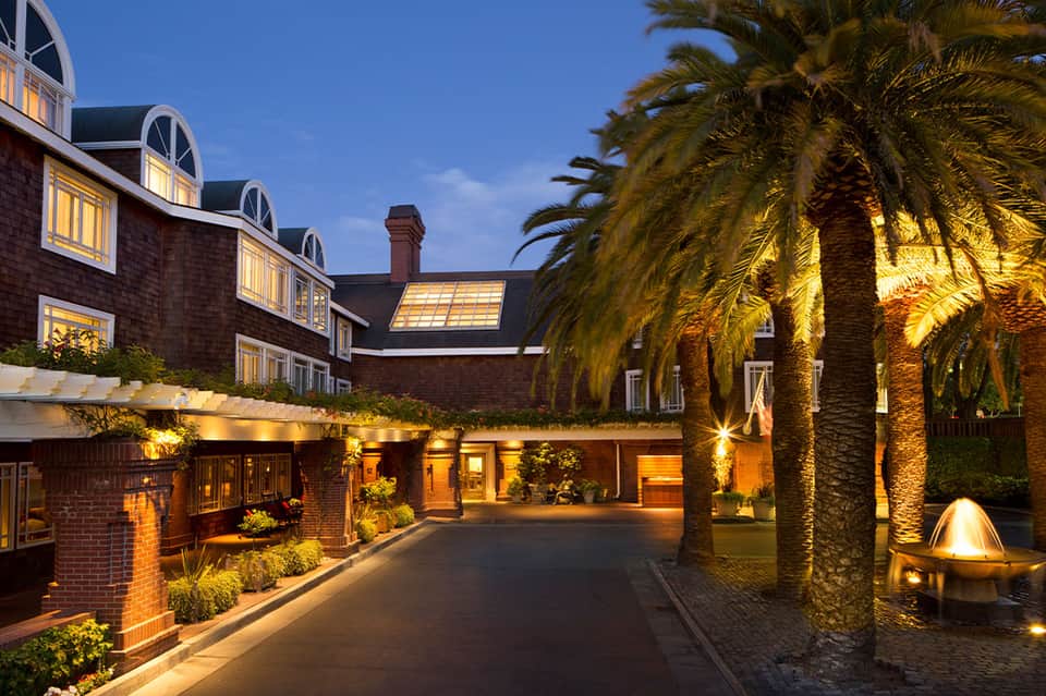 Illuminated brick hotel building at dusk with palm trees, dormer windows, and courtyard lighting