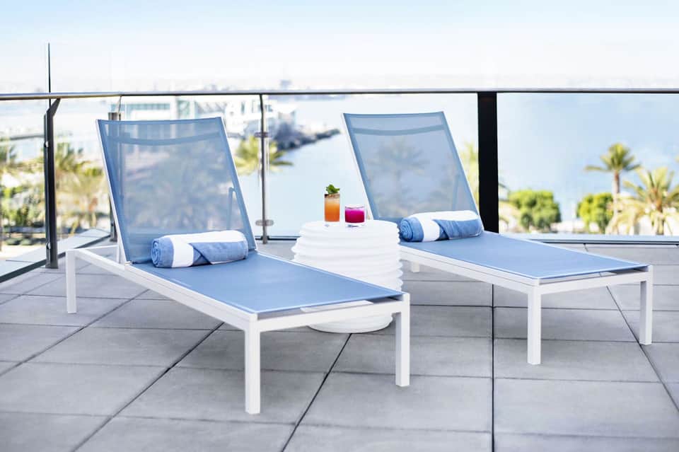 Rooftop lounge with two blue mesh chaise lounges overlooking palm trees and coastal city skyline