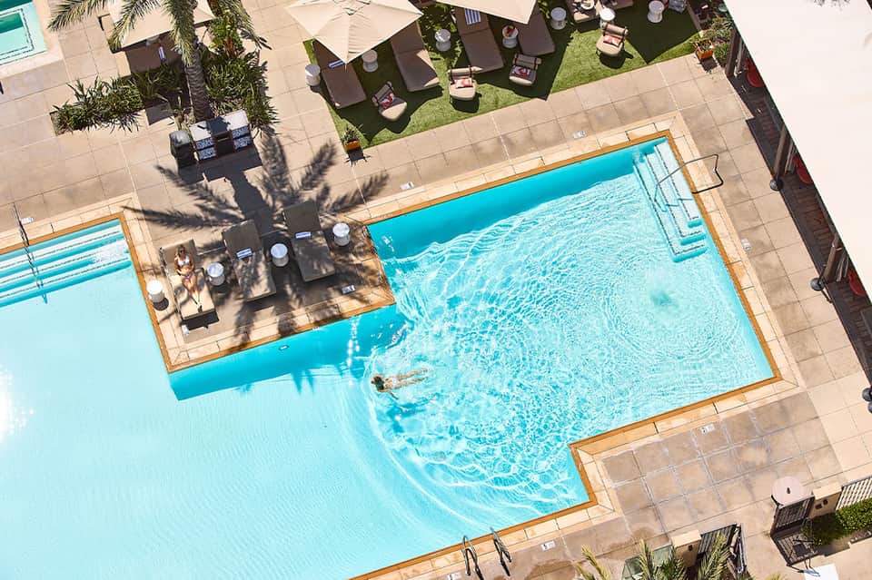 Overhead view of blue lap pool with spa, sun loungers, and palm tree shade