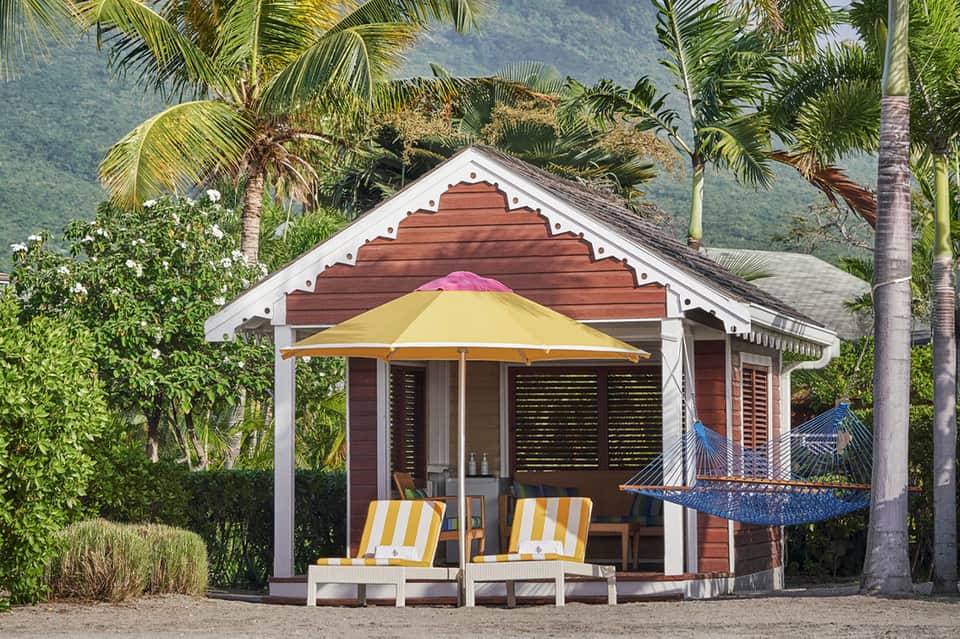 Tropical beachside cabana with red wood structure, yellow umbrella, and hammock with mountain views