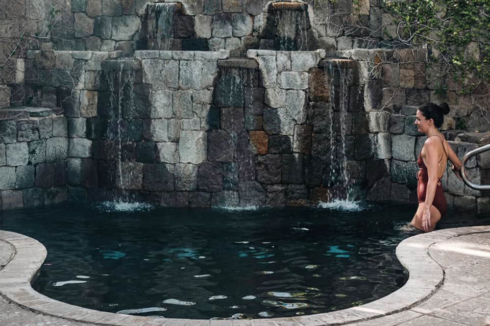 Woman in swimsuit at stone waterfall pool feature with cascading water