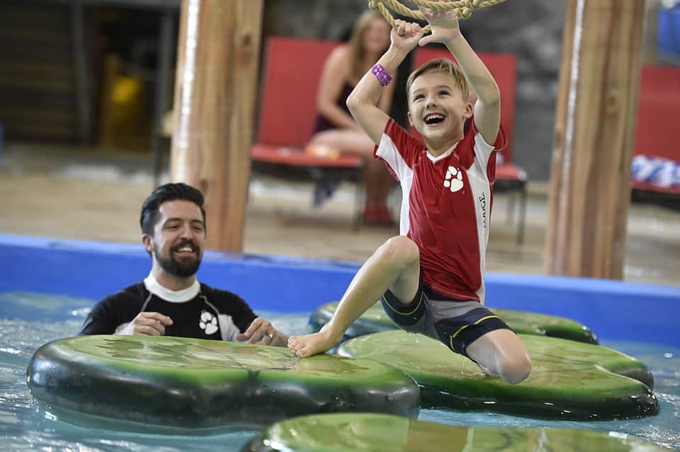 Young child on paddleboard in pool with instructor, laughing joyfully during lesson