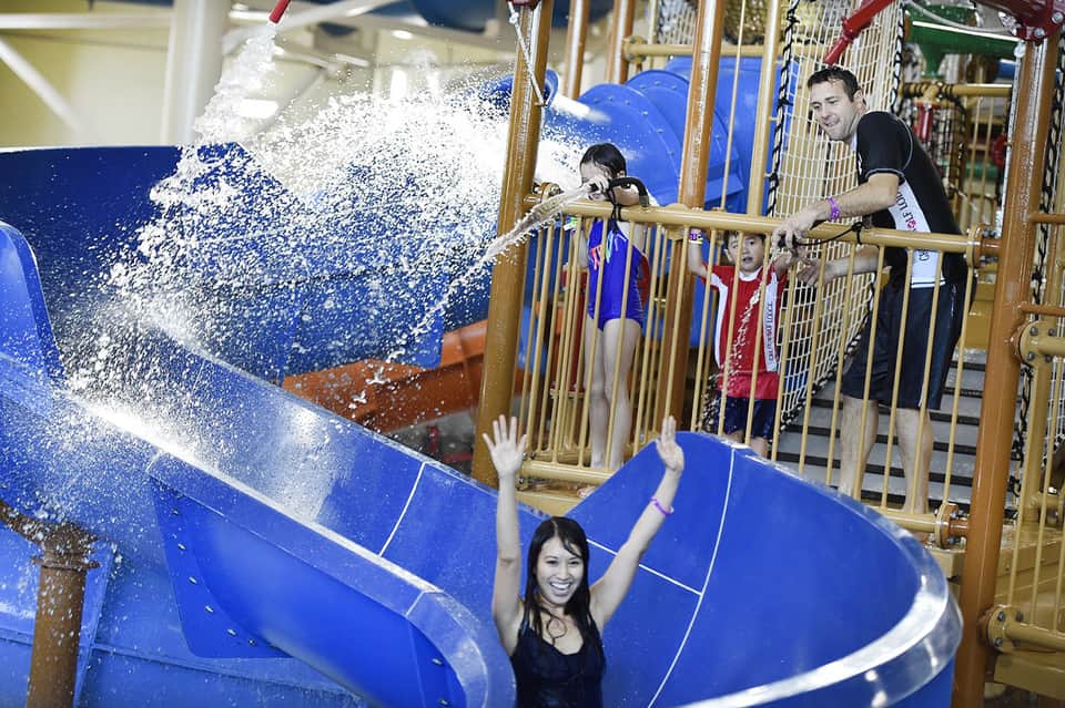 Indoor water park with children on blue water slide wearing safety gear
