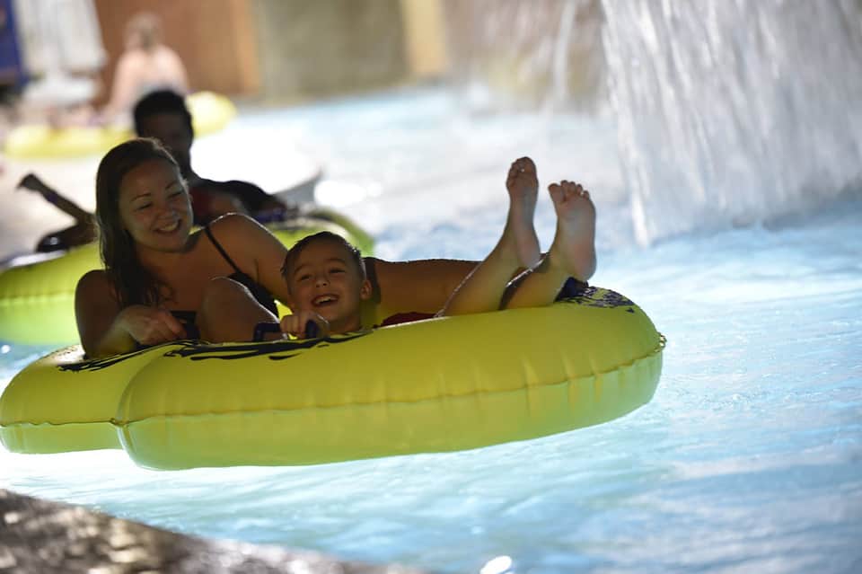 Mother and child laughing together on yellow inflatable tube in bright blue resort pool