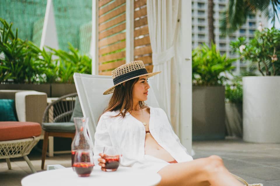 Woman in white shirt and hat relaxing on lounge chair on modern rooftop terrace with city views