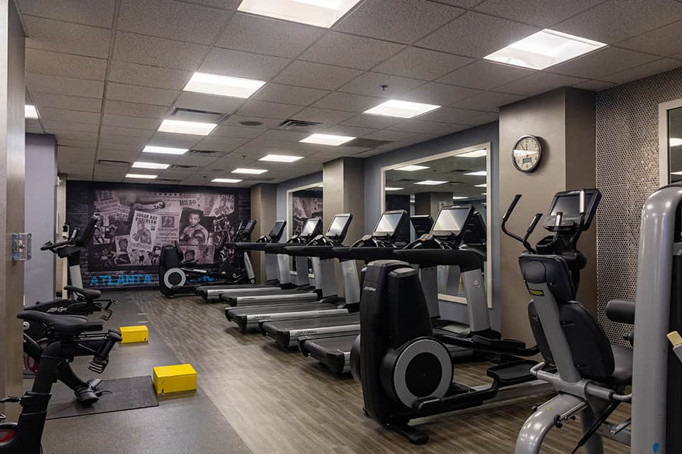 Modern fitness center with rows of treadmills, exercise bikes, mirrors, and Atlanta-themed wall art