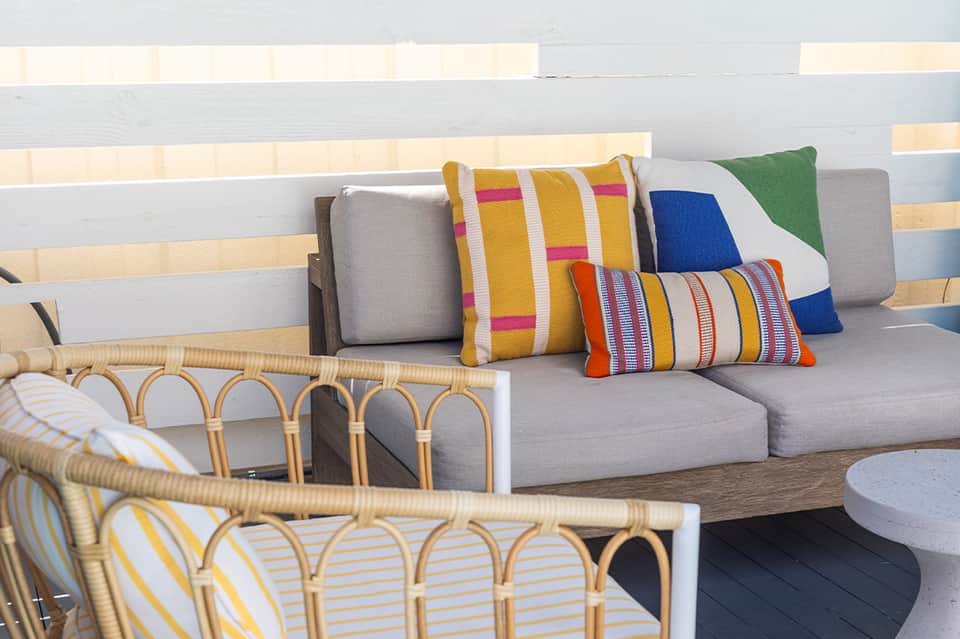 Outdoor seating area with wicker furniture, striped pillows in bright colors on gray cushions