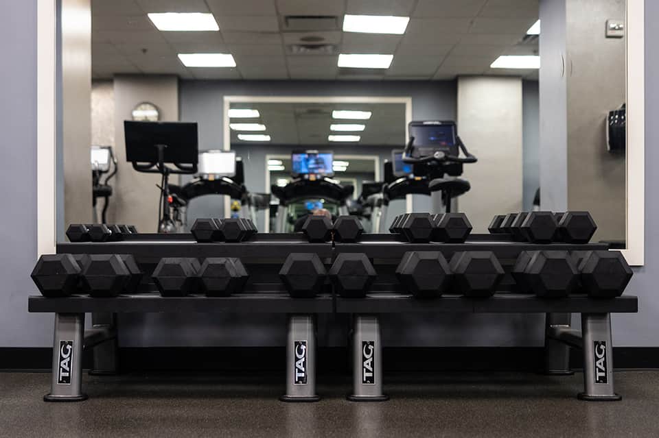 Fitness center with dumbbell racks and stationary bikes reflected in mirrors