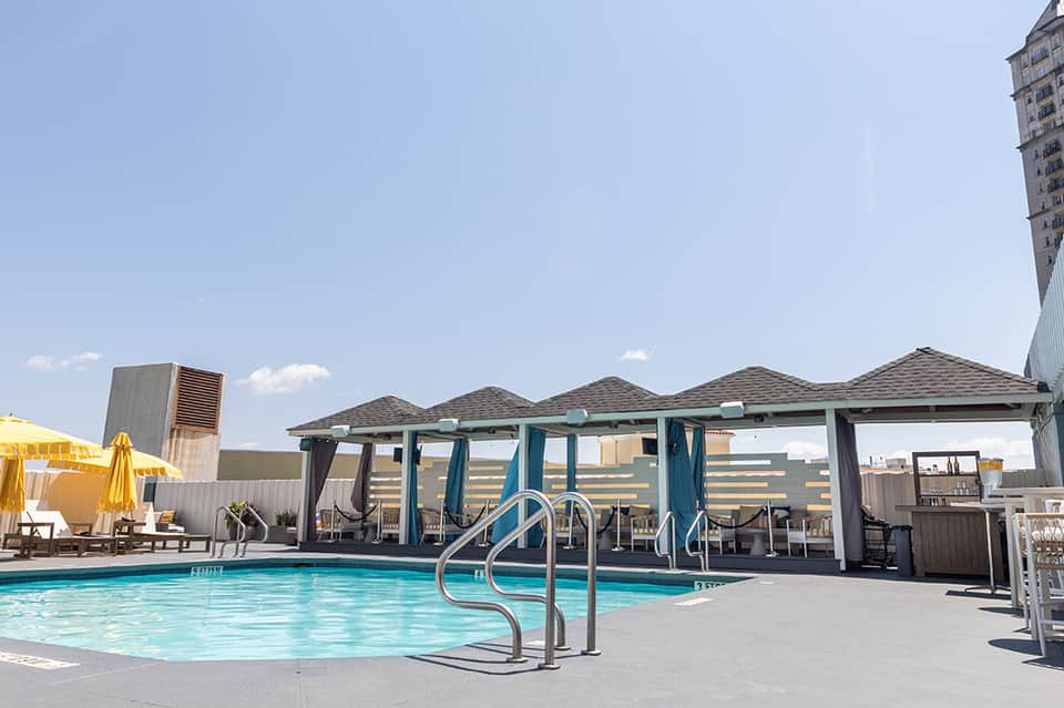 Rooftop pool with blue water, lounge chairs, cabanas, and city skyline in background