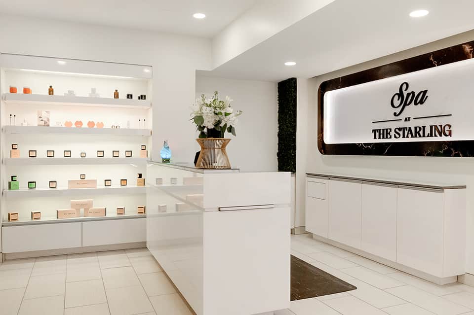 Spa reception area with white shelving displaying products, neon sign, and floral arrangement