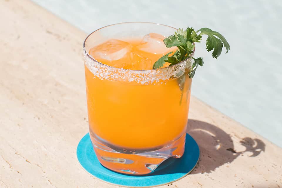 Orange cocktail with salt rim and fresh herbs garnish poolside on blue coaster