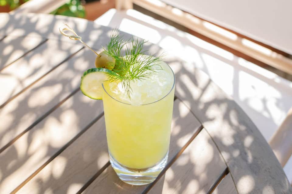 Refreshing yellow cocktail with lime slice and dill garnish on wooden deck table