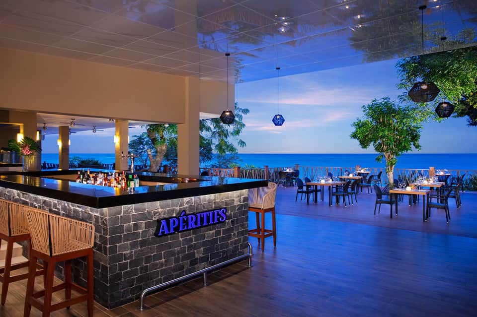 Oceanfront bar and dining area with blue lighting overlooking the sea at dusk